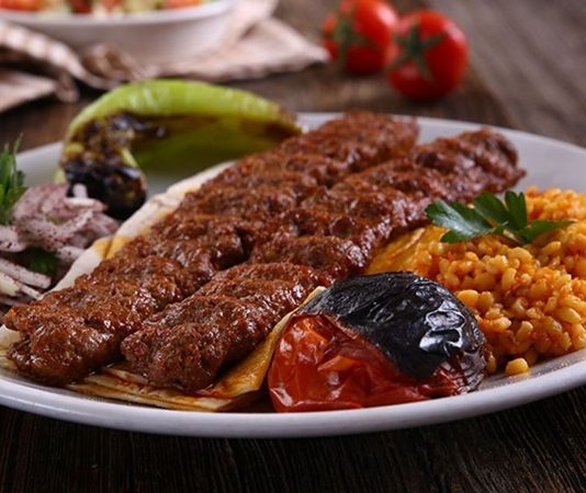 Kebap, Türk mutfağının en köklü ve en tanınan lezzetlerinden biri olarak, yalnızca bir yemek değil aynı zamanda bir yaşam biçimi olarak da değerlendirilebilir. Etin ateşle buluştuğu bu eşsiz teknik, binlerce yıllık geçmişe sahiptir ve tarih boyunca birçok uygarlığın mutfağında kendine yer bulmuştur. Ancak Anadolu toprakları, kebap kültürünü sadece korumakla kalmamış, aynı zamanda onu çeşitlendirip zenginleştirmiştir. Konulu bir haber görseli.