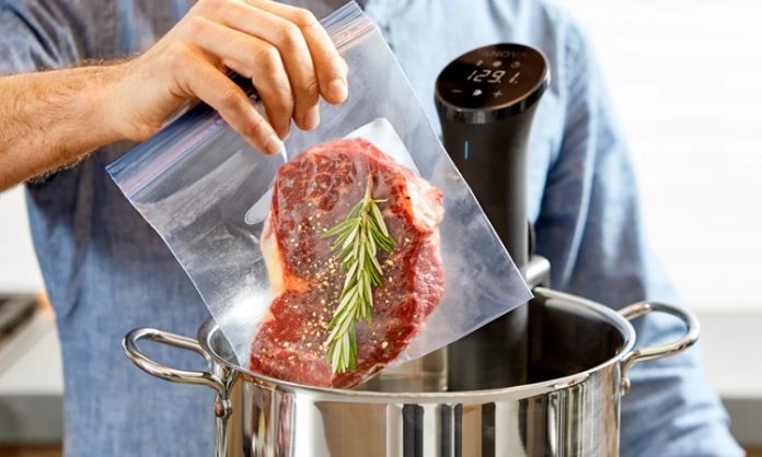 Sous Vide Yöntemiyle Yemeklerde Mükemmel Lezzet Sous vide Fransızca’da “vakum altında” anlamına gelen bir pişirme tekniğidir. Yiyecekler özel poşetlerin içine yerleştirilip vakumlanır ve ardından kontrollü bir şekilde düşük sıcaklıkta su banyosunda pişirilir. Bu yöntem 1970’li yıllarda profesyonel şefler tarafından keşfedilmiş ve zamanla restoran mutfaklarından ev mutfaklarına kadar yayılmıştır. Özellikle et, balık ve sebzelerde istenen pişirme derecesine ulaşmayı kolaylaştırdığı için tercih edilmektedir. Konulu bir haber görseli.