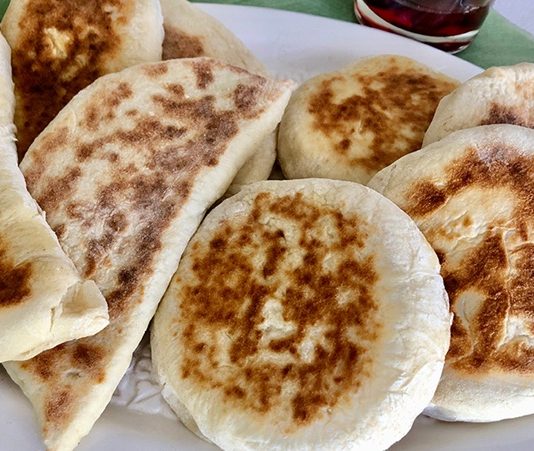 Bazlama: Gelenekten Sofralara Uzanan Sıcak Lezzet Türk mutfağının en özel ve sevilen ekmek çeşitlerinden biri olan bazlama, yumuşak dokusu, doyurucu yapısı ve mis gibi kokusuyla sofraların vazgeçilmezidir. Özellikle Anadolu’nun birçok bölgesinde kahvaltıların, çay saatlerinin ve hatta ana yemeklerin yanında sıklıkla tercih edilen bu ekmek, sadece lezzetiyle değil kültürel bir değer olarak da öne çıkar. Günümüzde modern sofralarda da kendine yer bulan bazlama, hem geleneksel hem de pratik bir lezzet olarak dikkat çekmektedir. Konulu bir haber görseli.