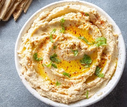 Humus: Lezzetiyle Sofraların Vazgeçilmez Mezesi Humus, Orta Doğu mutfağının en bilinen ve sevilen mezelerinden biridir. Başlıca malzemeleri nohut, tahin, limon suyu, sarımsak ve zeytinyağı olan bu özel tarif, yüzyıllardır sofralarda yerini almaktadır. Tarihi çok eski dönemlere dayanan humus, özellikle Lübnan, Suriye, Filistin ve Türkiye gibi bölgelerde yaygın olarak tüketilir. Bugün ise dünya genelinde sağlıklı bir atıştırmalık ya da ana yemek yanında tamamlayıcı olarak tercih edilmektedir. Konulu bir haber görseli.