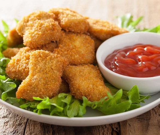 Nugget: Pratik Atıştırmalıkların Lezzetli Tercihi Nugget, özellikle hızlı ve pratik öğün arayanların favori seçeneklerinden biri haline gelmiş bir yiyecektir. Kökeni Amerika’ya dayanan bu atıştırmalık, 1950’li yıllarda geliştirilmiş ve kısa sürede dünya çapında popüler olmuştur. Tavuk eti, kaplamalı ve kızartılmış olarak hazırlanarak altın sarısı bir dış yüzeye kavuşur. Konulu bir haber görseli.