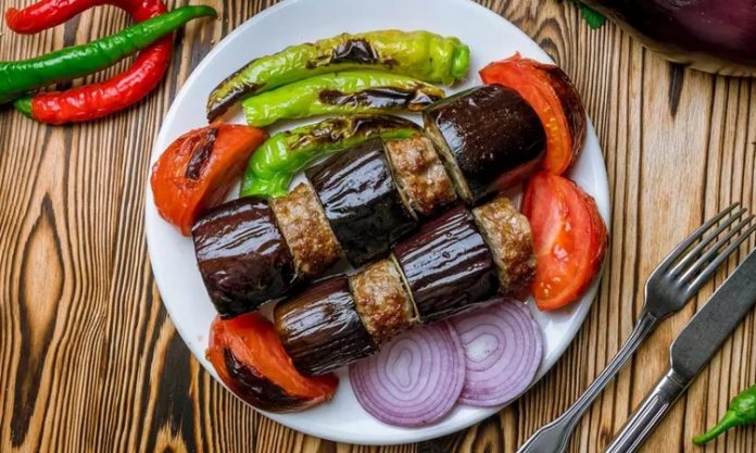 Patlıcan Kebabı Sofraların Lezzetli ve Geleneksel Yemeği Türk mutfağının vazgeçilmez lezzetlerinden biri olan patlıcan kebabı, özellikle Gaziantep, Şanlıurfa ve Adana gibi şehirlerde sıkça hazırlanır. Patlıcanın közlenip etle buluşmasıyla ortaya çıkan bu yemek, hem hafif hem de doyurucu bir öğün sunar. Osmanlı mutfağından günümüze uzanan tarif, yöresel farklılıklarla her sofrada kendine özgü bir tat bırakır. Konulu bir haber görseli.