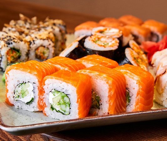 Sushi roll, Japon mutfağının en bilinen yemeklerinden biridir ve dünya genelinde ün kazanmıştır. İlk olarak Edo döneminde ortaya çıkan sushi, başlangıçta balığın pirinç içinde fermente edilmesiyle hazırlanıyordu. Zaman içinde bu yöntem değişti ve daha modern bir hale geldi. Özellikle 20. yüzyılın ortalarında Amerika’da popülerleşen sushi roll, farklı malzemelerin bir araya gelmesiyle çeşitlenerek bugünkü halini aldı. Konulu bir haber görseli.