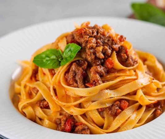 Tagliatelle: İtalyan Mutfağının İnce Şerit Makarna Lezzeti Tagliatelle, İtalyan mutfağının en tanınmış makarna çeşitlerinden biri olarak bilinir. Genellikle geniş ve uzun şeritler halinde hazırlanır. Bu makarna türü, özellikle Bolognese sosu ile eşsiz bir uyum yakalar ve İtalya’nın Emilia-Romagna bölgesinde köklü bir geçmişe sahiptir. Konulu bir haber görseli.