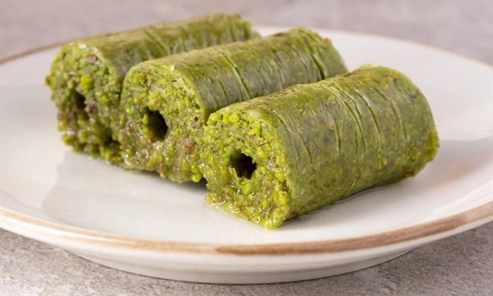 Gaziantep mutfağıyla özdeşleşen fıstık sarma, son yıllarda hem Türkiye’de hem de dünya genelinde gastronomi meraklılarının dikkatini çeken özel tatlılardan biri hâline geldi. İncecik açılan kadayıf hamurunun arasına bolca Antep fıstığı eklenerek hazırlanan bu eşsiz tatlı, hem görünümüyle hem de yoğun aromasıyla öne çıkıyor. Tatlı severlerin ilgisini çeken en önemli özelliklerinden biri ise tamamen doğal malzemelerle hazırlanmasına rağmen oldukça rafine bir lezzet sunması. Üstelik geleneksel tarifin modern dokunuşlarla birleşmesi, fıstık sarmayı son dönemde gurme restoranların da vazgeçilmezi yapıyor. Konulu bir haber görseli.